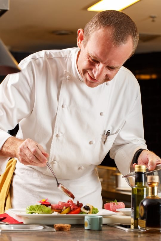Portrait of chef flambéing a dish in a professional kitchen, styled for a fine dining branding shoot