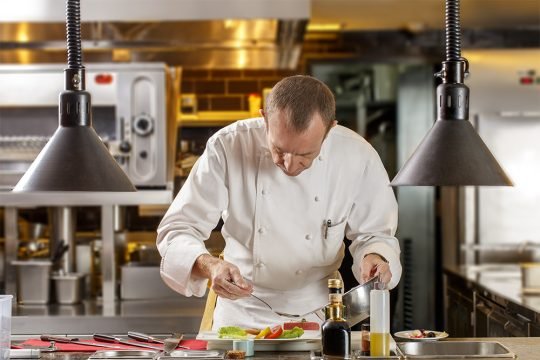 Close-up portrait of chef adding final touches to a meal, captured for a culinary brand campaign