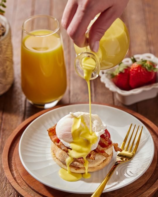 Close-up of a beautifully plated egg benedict and seasonal fruits, captured for a restaurant menu