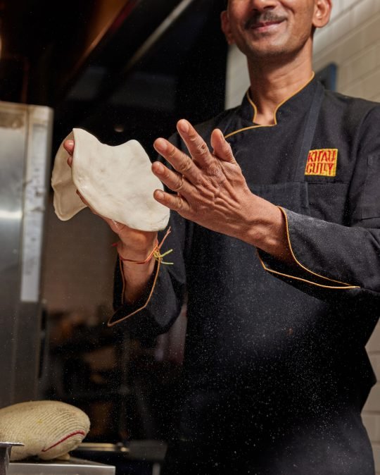Profile portrait of a smiling man in kitchen making a nan bread, photographed for magazine project