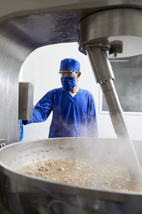 Portrait of a factory technician inspecting products on an assembly line, photographed in a large industrial facility