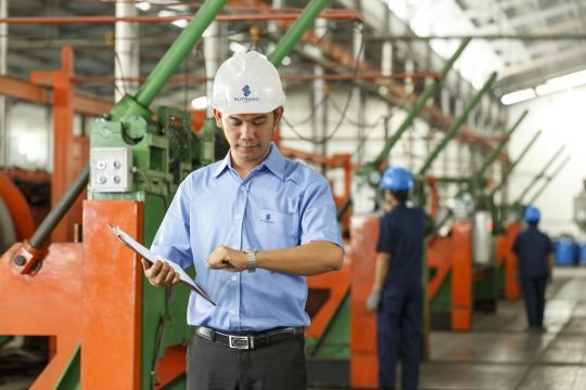 Portrait of a factory technician inspecting products on an assembly line, photographed in a large industrial facility