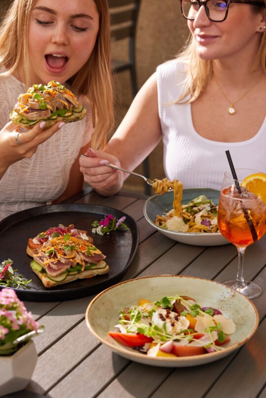 Two friends sitting in the outdoor setting enjoy, chatting, eating in the bright summer light