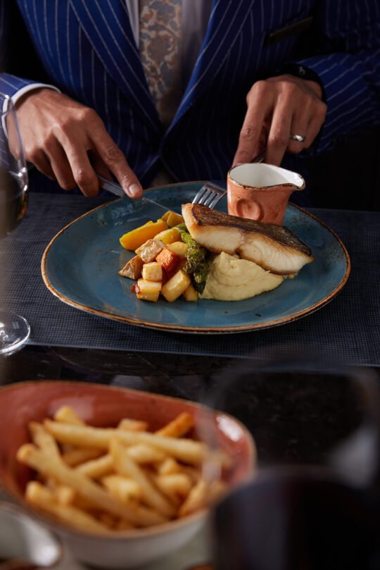 A couple having a dinner together in Natural light, focus on the man's had cutting the food in front him. moody atmosphere capture the feeling of a perfect dining moment.