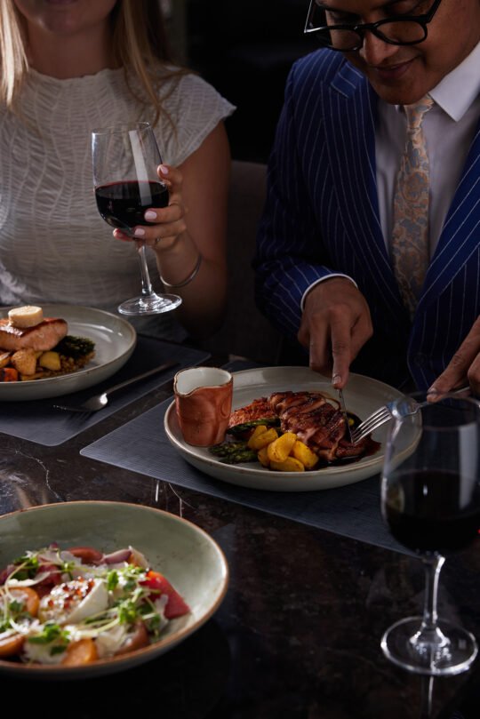 A couple sitting side by side having a dinner together in Natural light, moody atmosphere capture the feeling of a perfect dining moment.