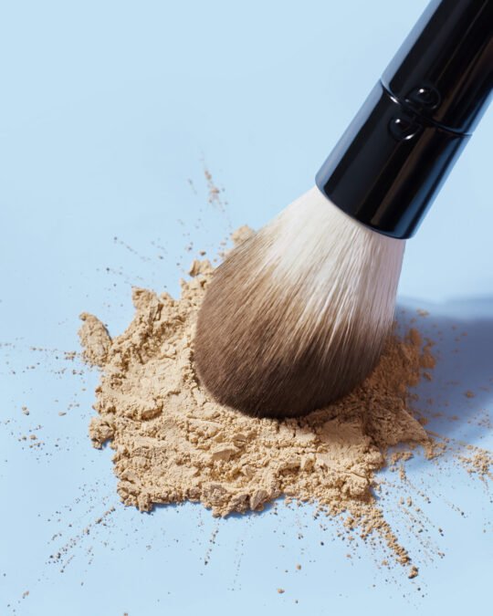 Commercial product photography of a make up brush and the powder make up spread on blue background