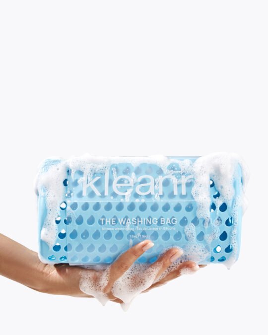 Commercial product photography of woman's hand holding a blue washing bag with foam and bubbles on it on a white background.