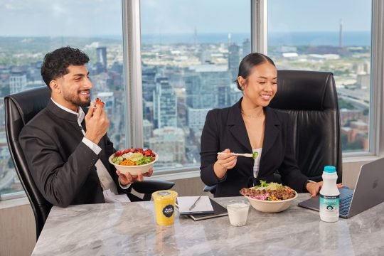 Office employees eating together at a communal table, styled for a workplace wellness campaign
