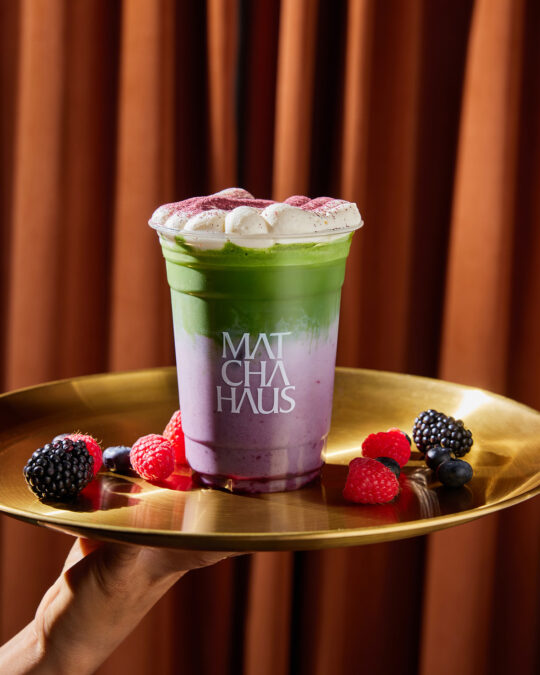 A Berry Matcha photograph against curtain rose gold background on the tray where hand serve as a premium drink