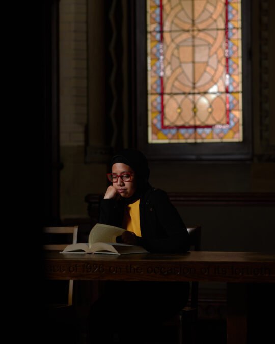Portrait of Woman in dark sitting reading a book historic building in background - moddy lighting